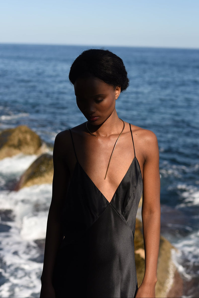 Woman wearing beautiful fine delicate but statement choker of 3 mm thick. Sain black dress on a rock.