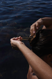 Woman securing wet hair with the sculptural gold Delos hair pin by MVDT Collection.