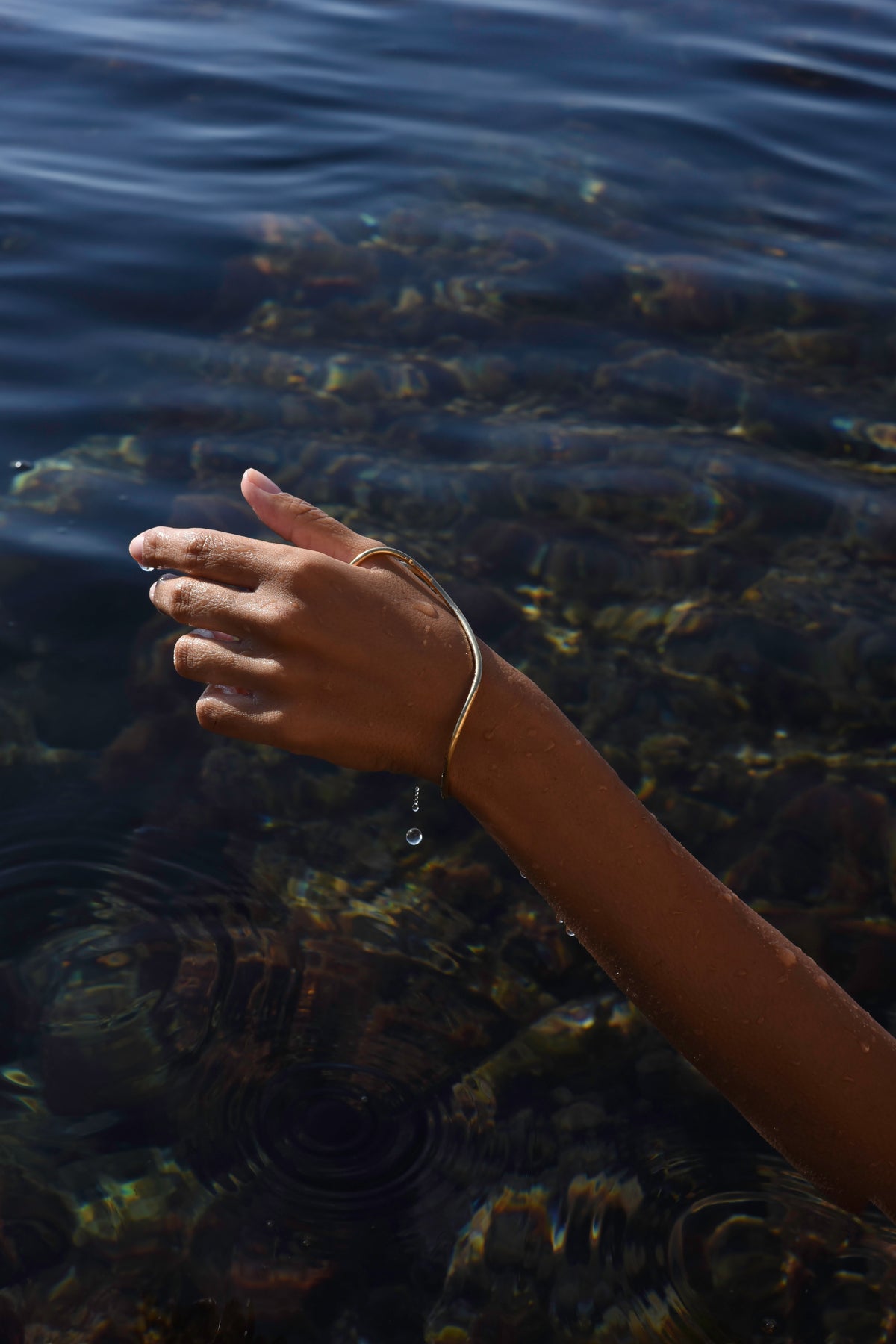Gold Delos handmade thumb hand bracelet worn over the hand beside the Mediterranean Sea.