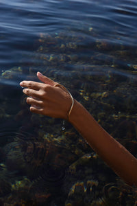 Gold Delos handmade thumb hand bracelet worn over the hand beside the Mediterranean Sea.